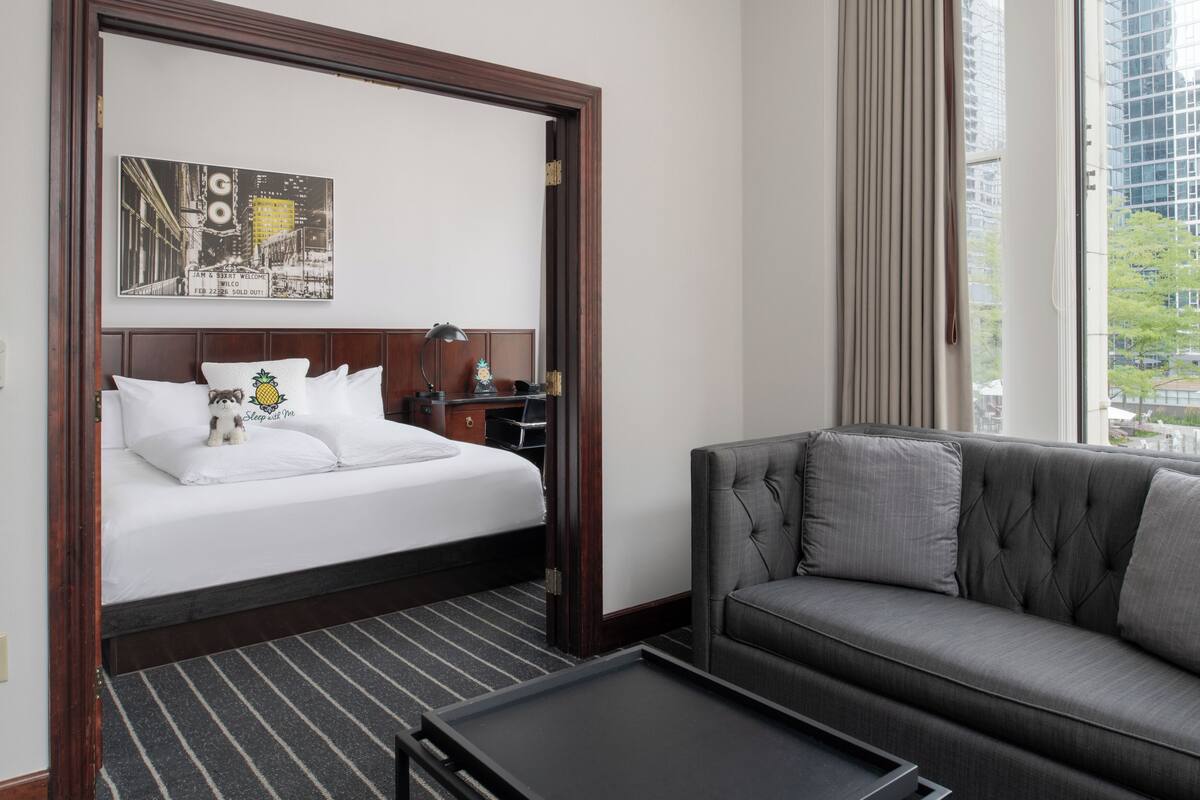 A hotel room with a bed, a sofa, a desk, and a window with a city view.