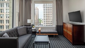 Una habitación de hotel moderna con sofá, una mesita, un banco, televisor y un armario.