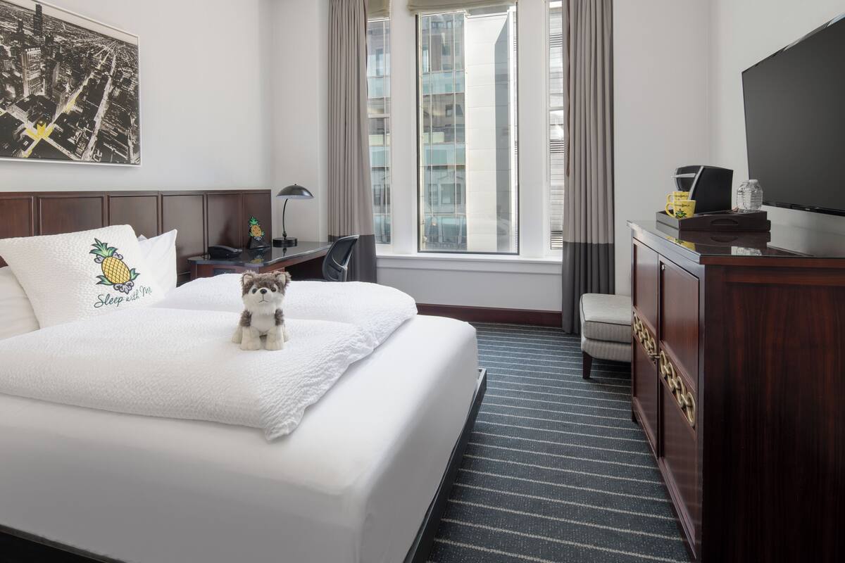 A hotel room with a large bed, a desk, a chair, a TV, and a window with curtains.