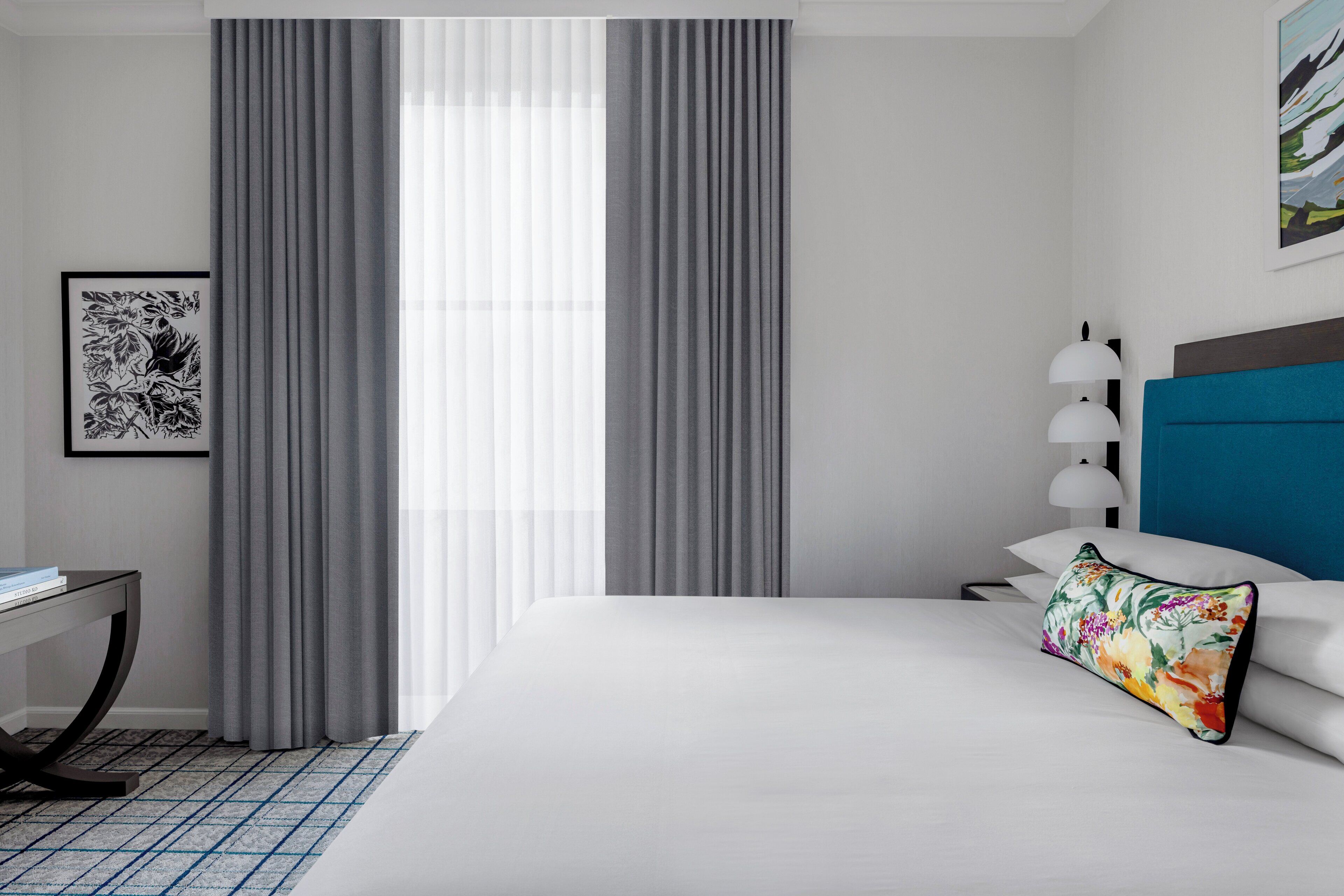 A hotel room with a bed, a desk, a lamp, and a window with curtains.