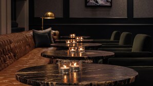 A dimly lit lounge area with leather seating and round tables, each with a lit candle.