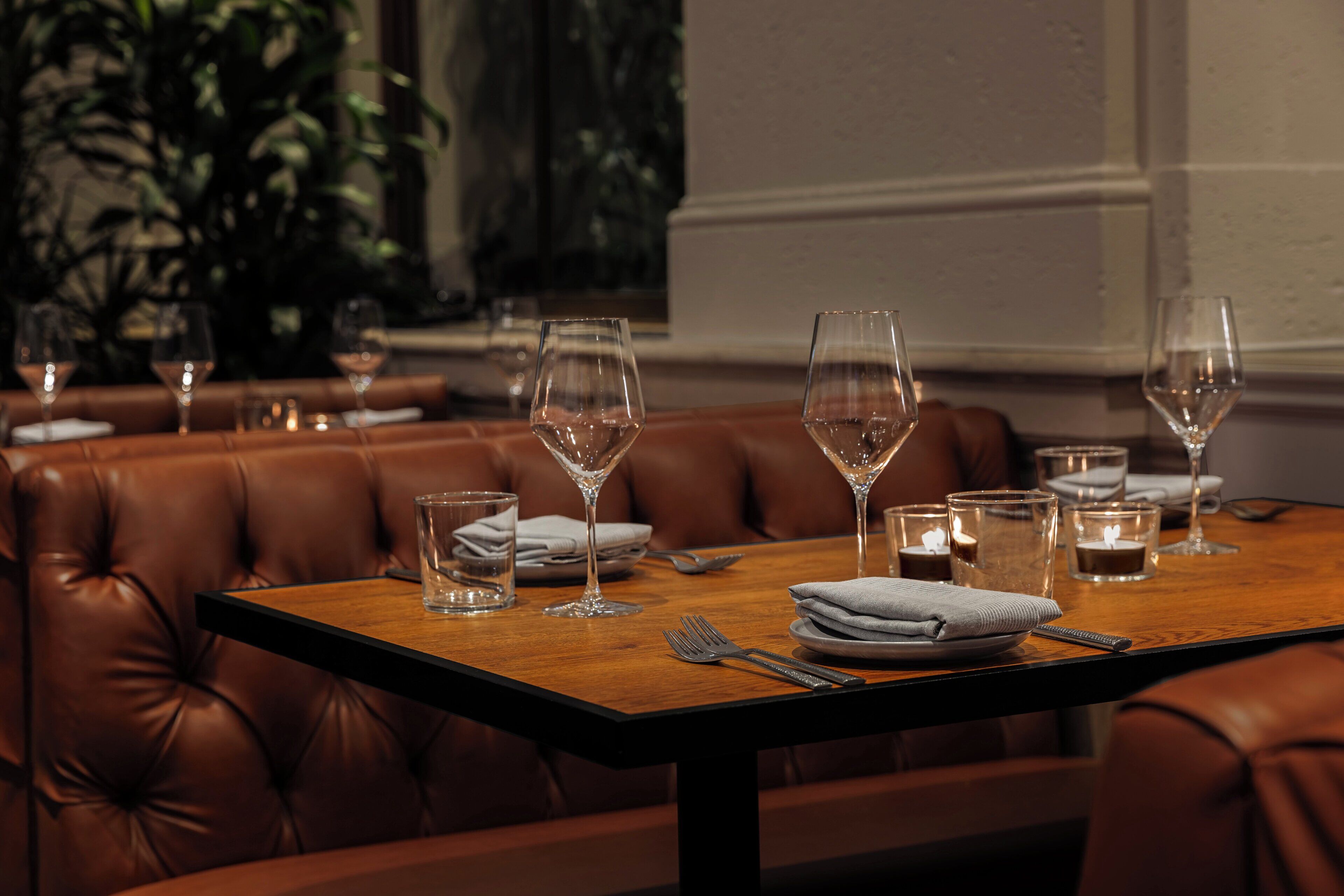 A dining table set with wine glasses, plates, and cutlery, surrounded by leather booth seating.