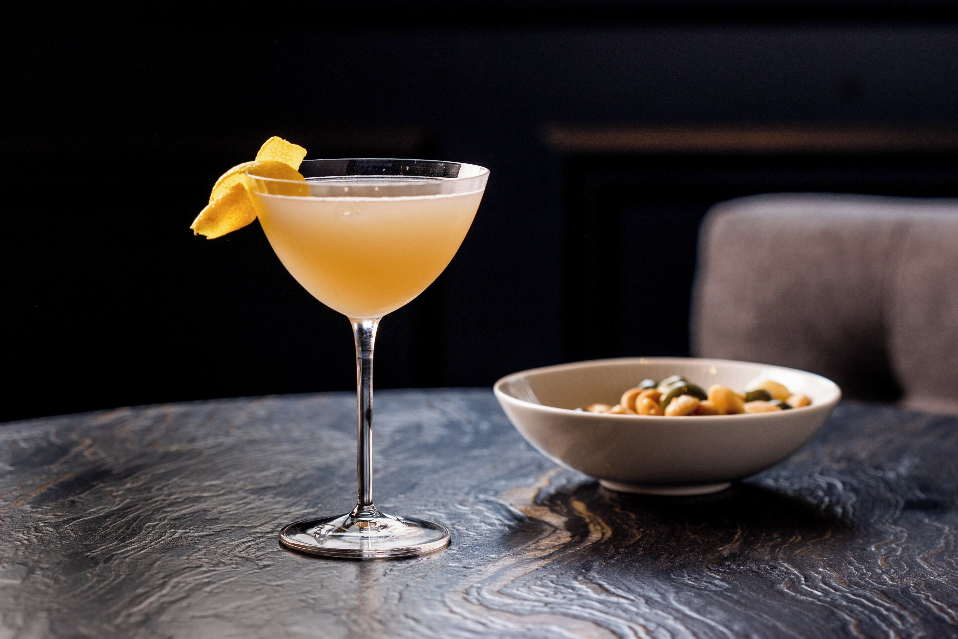 Una copa de martini con una rodaja de limón sobre una mesa de madera oscura.