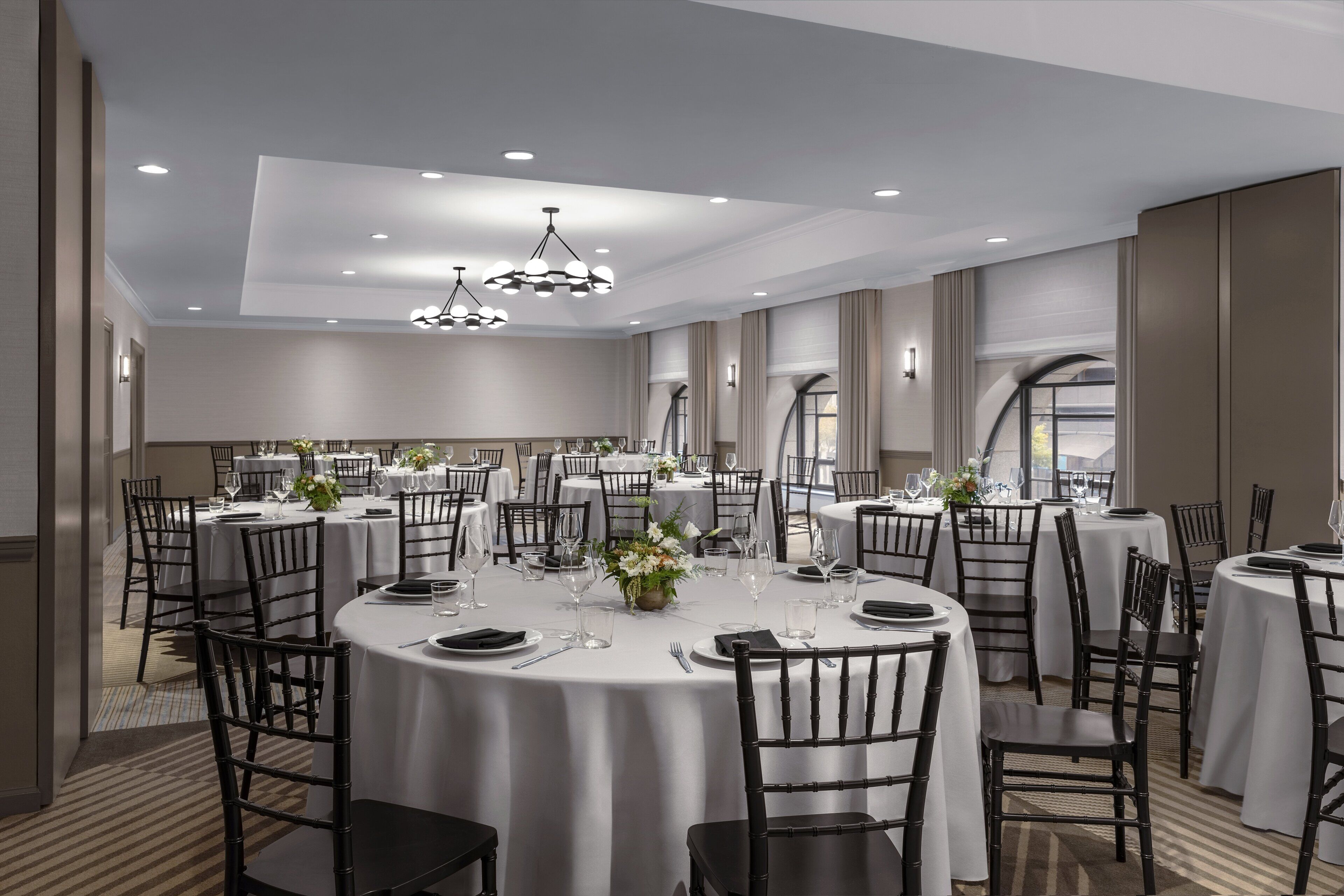 A spacious dining area with round tables, black chairs, and overhead lighting.