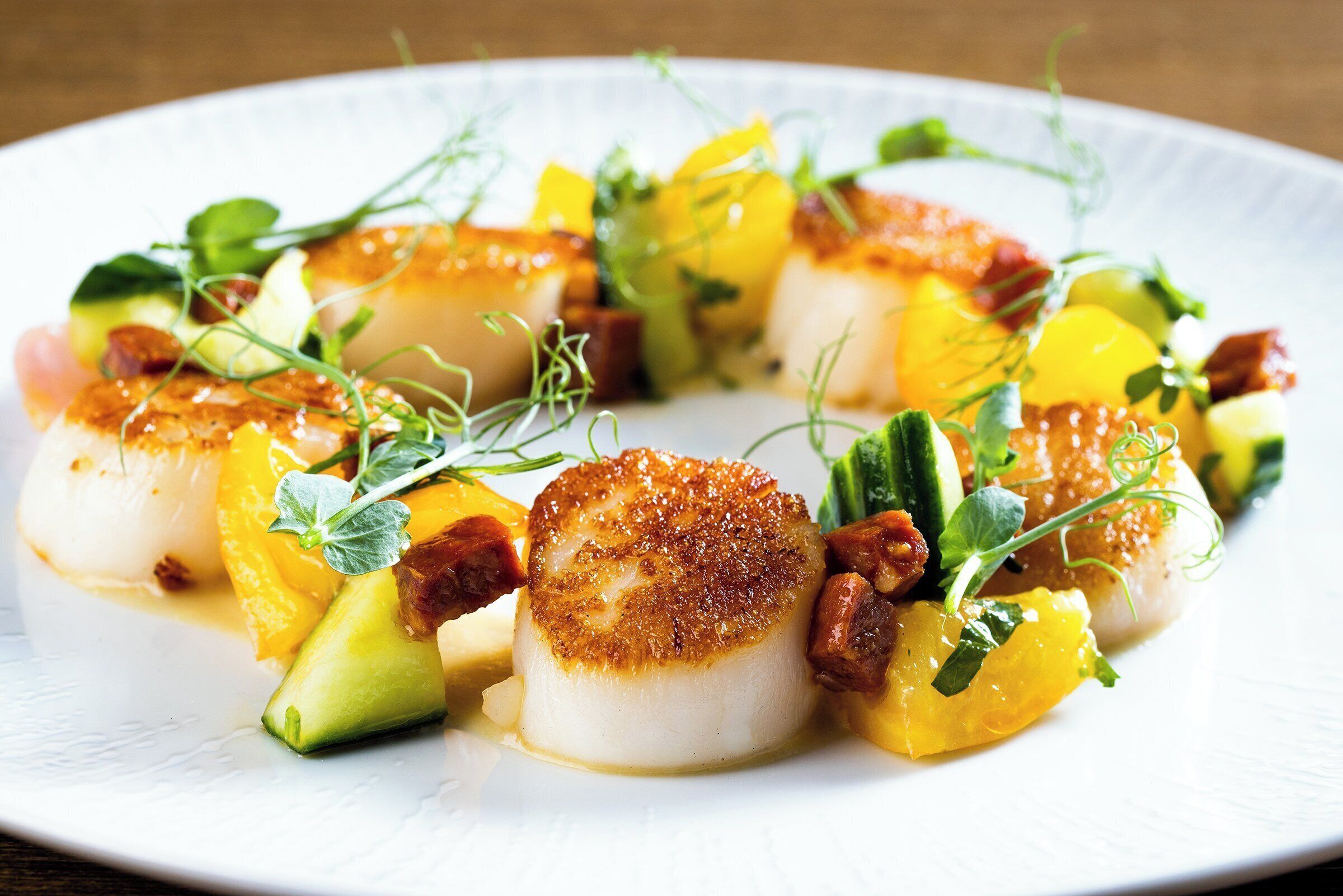 A plate of seared scallops with vegetables and herbs.