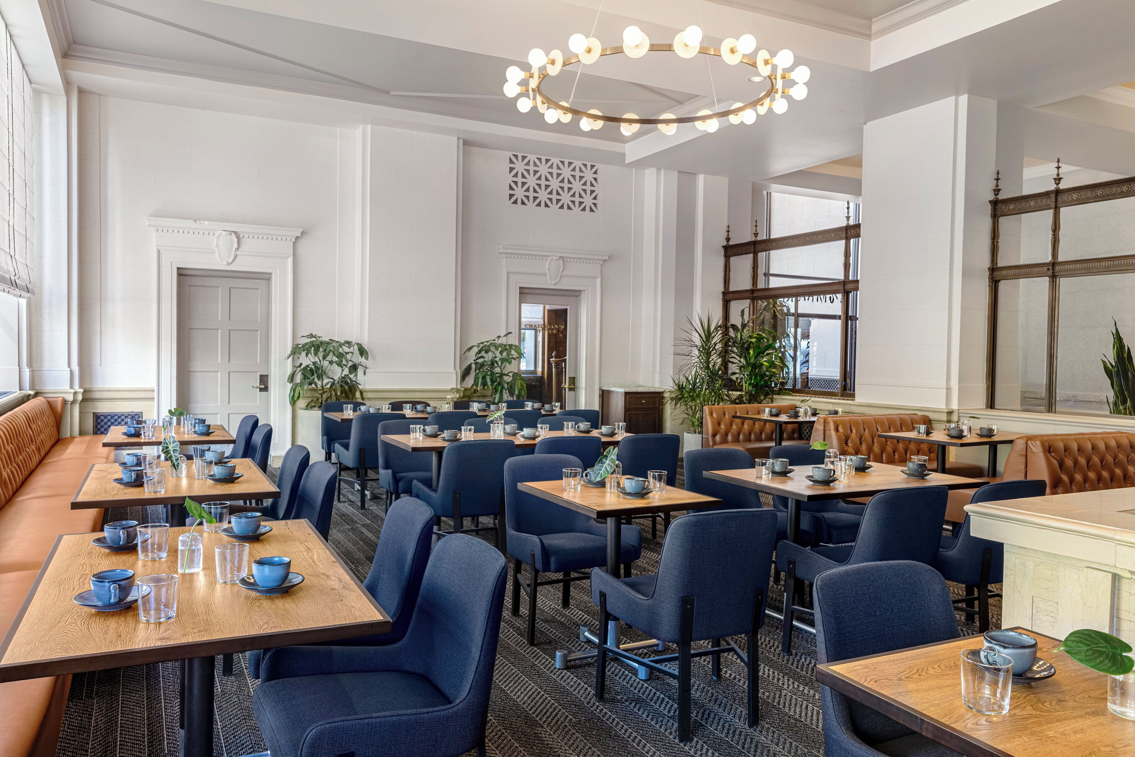 A hotel dining area with multiple tables and chairs, a chandelier, and a large mirror.