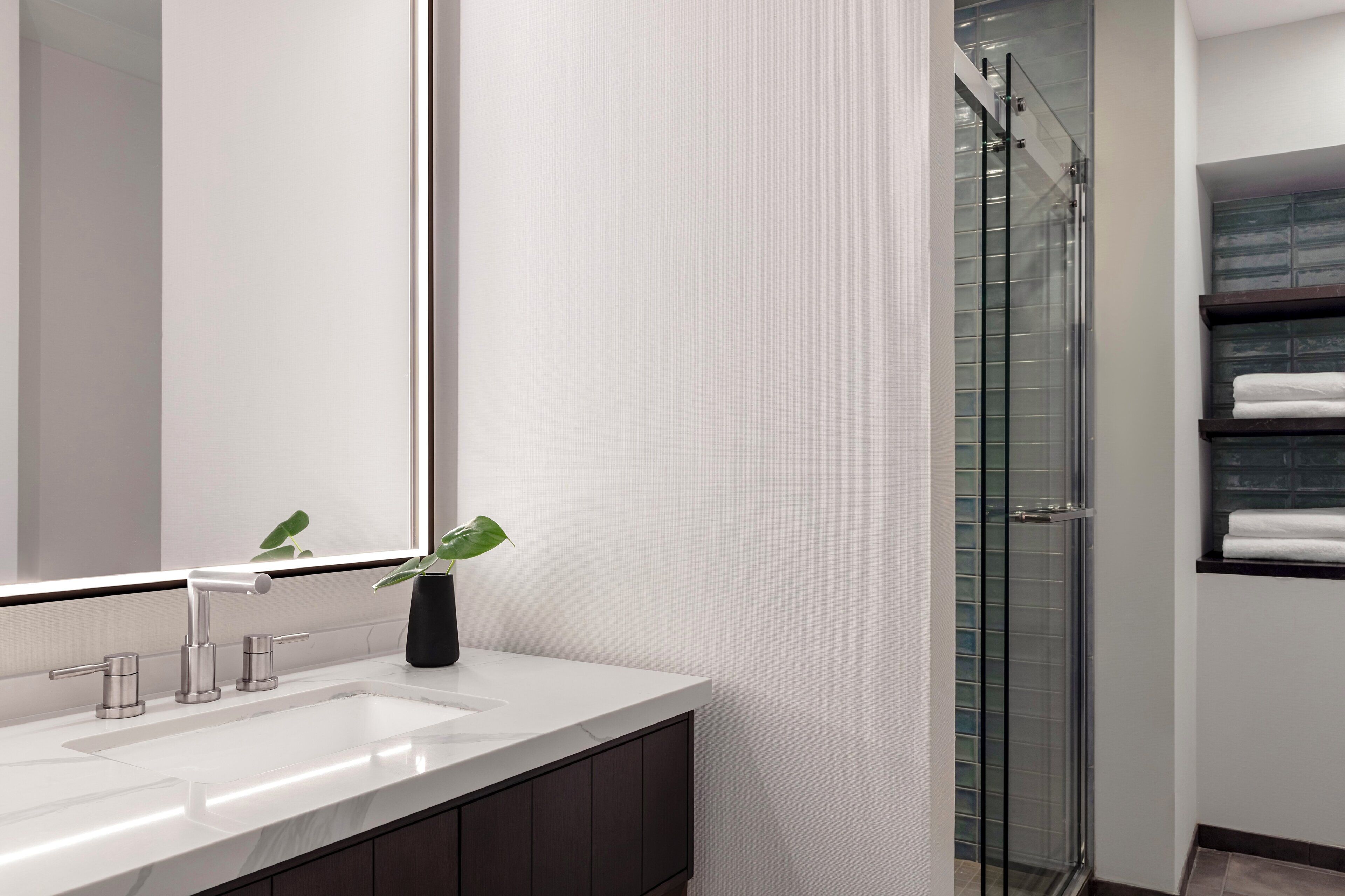 A modern bathroom with a white sink, a large mirror, and a glass shower enclosure.