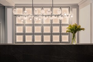 A modern interior with a marble countertop, a wall-mounted light fixture, and a vase with flowers.