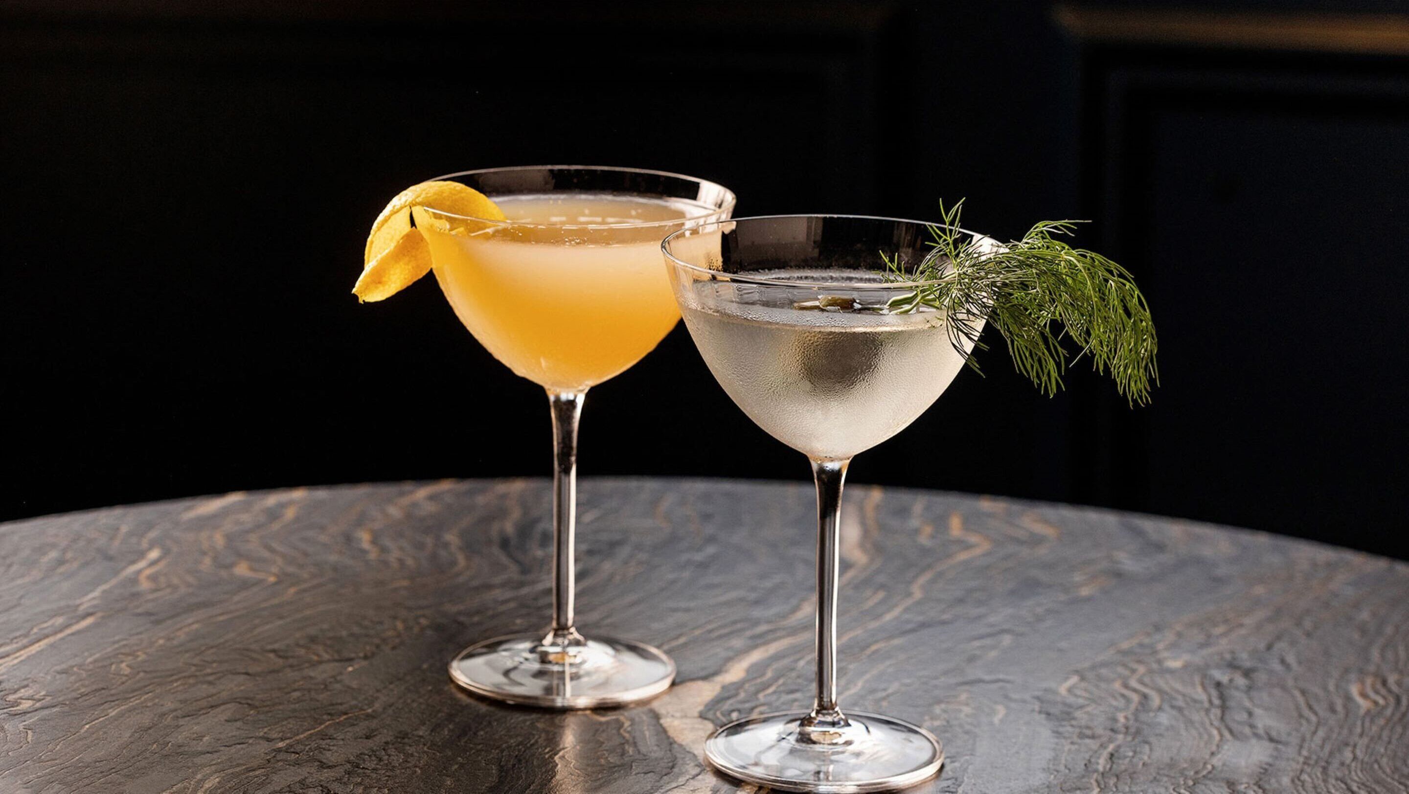 Two cocktails on a textured table with a dark background.