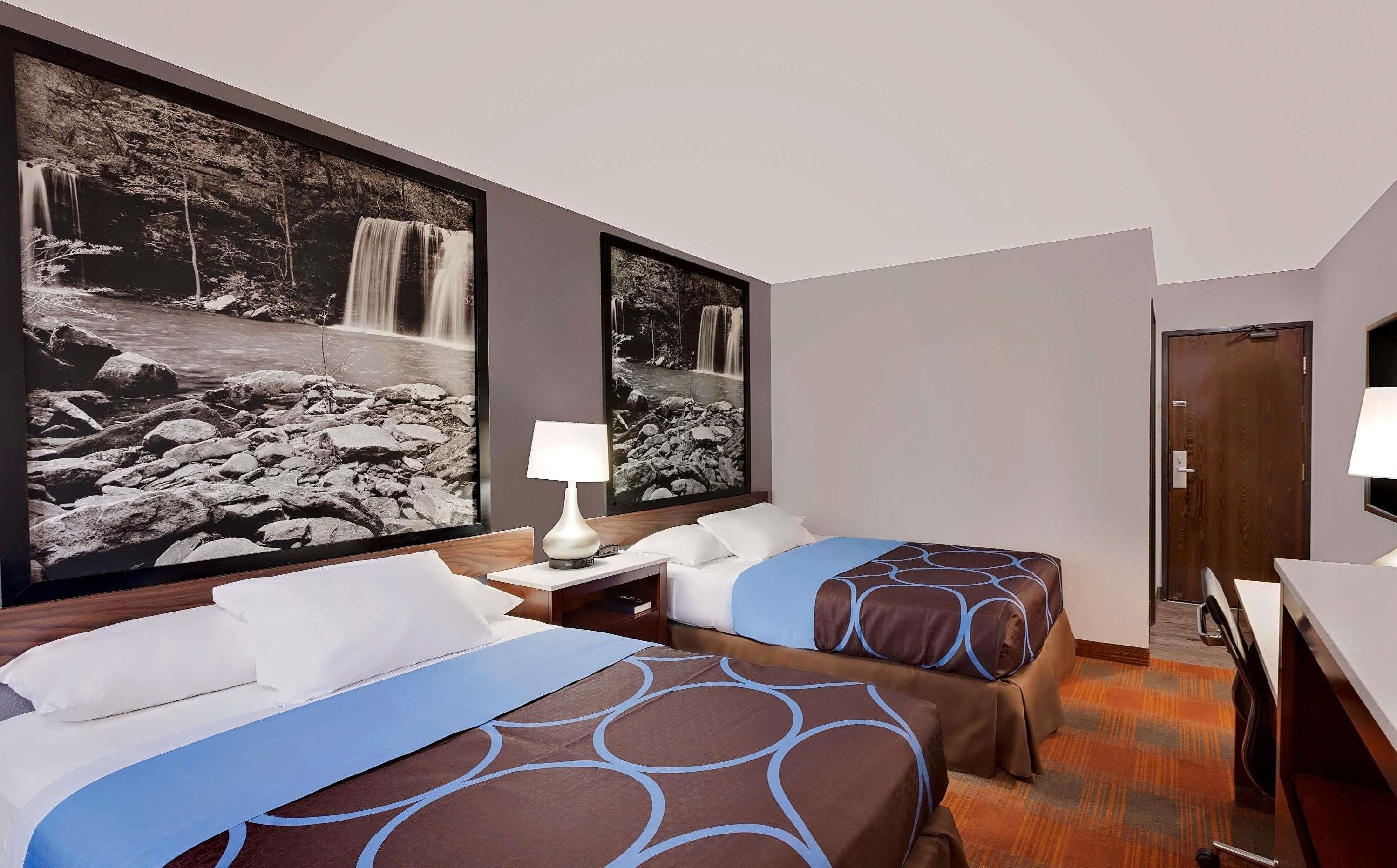 Hotelkamer met twee bedden, een bureau, een stoel en twee grote foto’s van watervallen aan de muur.