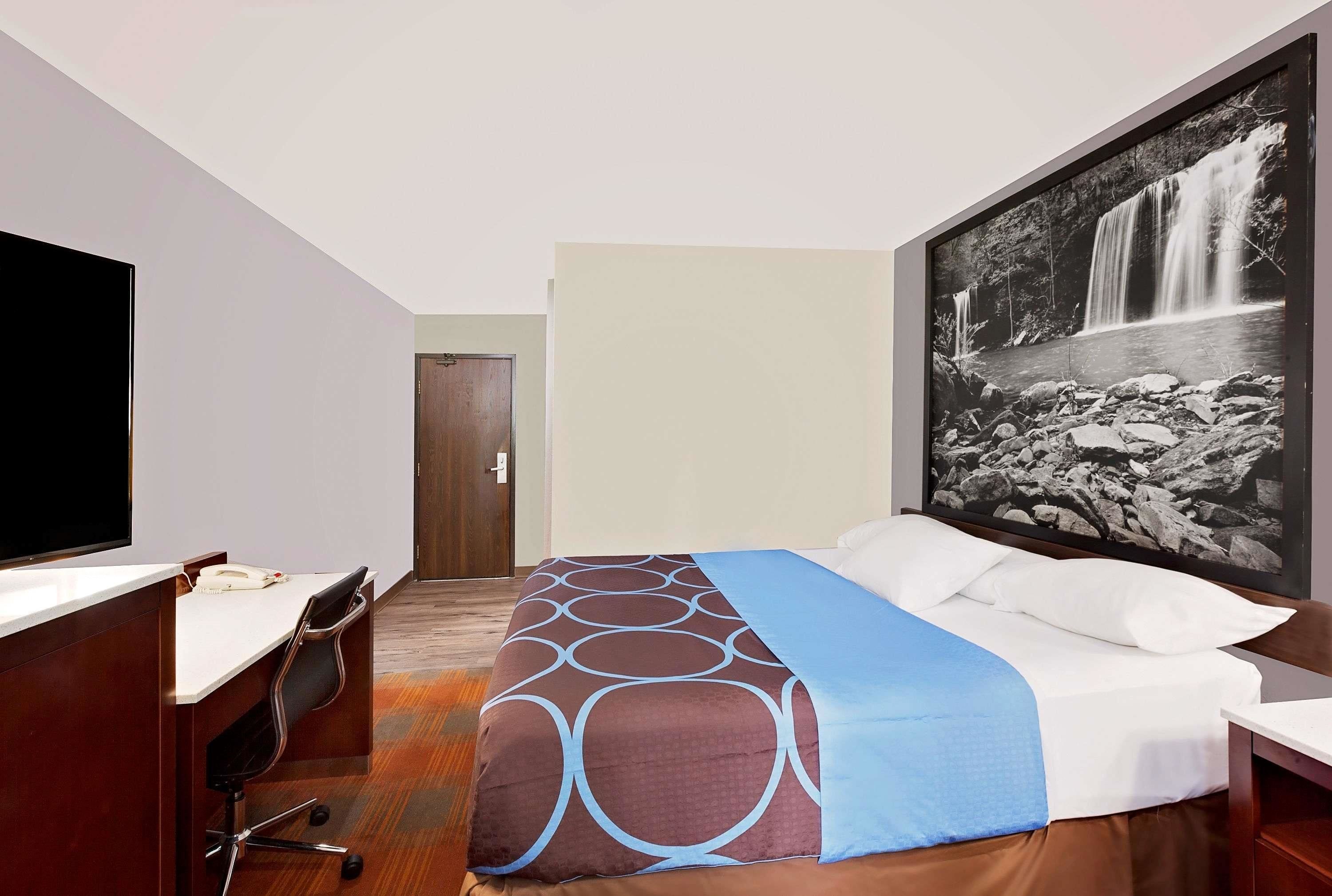 A hotel room with a bed, a desk, a chair, and a large framed picture of a waterfall.