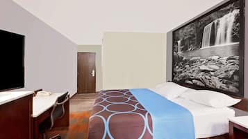 A hotel room with a bed, a desk, a chair, and a large framed picture of a waterfall.