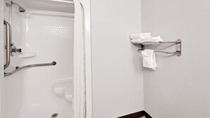 Un baño con ducha, barras de apoyo, toallero y retrete.