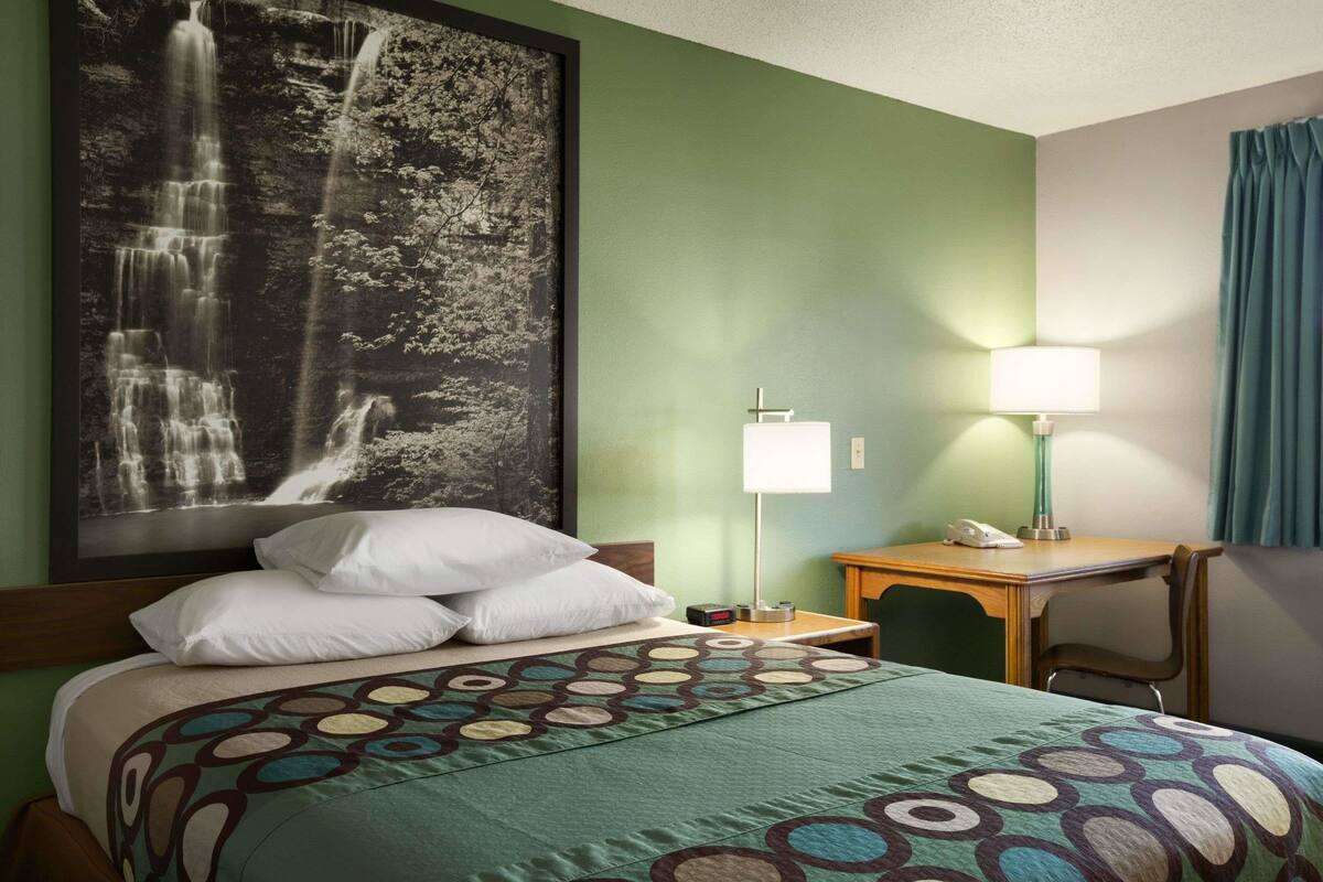 A hotel room with a bed, a desk, a chair, a lamp, and a large framed picture of a waterfall.