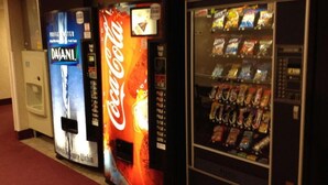 En rad med försäljningsautomater med olika märken, inklusive Coca-Cola, och ett kylskåp.