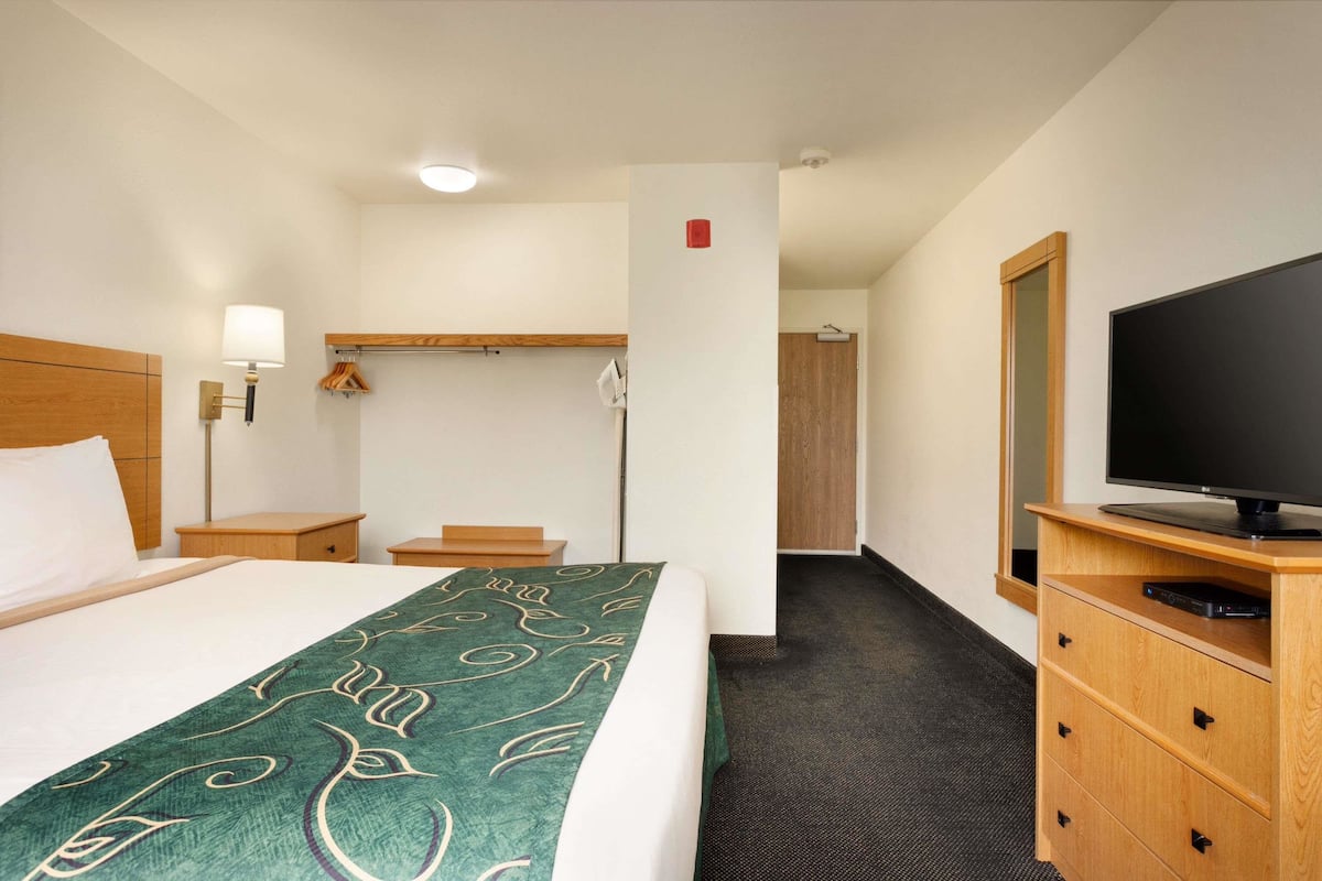 A hotel room with a bed, a TV on a wooden stand, a coat rack, and a door leading to another room.