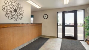 A reception area with a wooden counter, a decorative metal wall piece, a clock, and a large glass door leading outside.