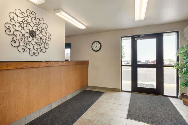 Un área de recepción con un mostrador de madera, un elemento decorativo de metal en la pared, un reloj y un gran ventanal que da al exterior.