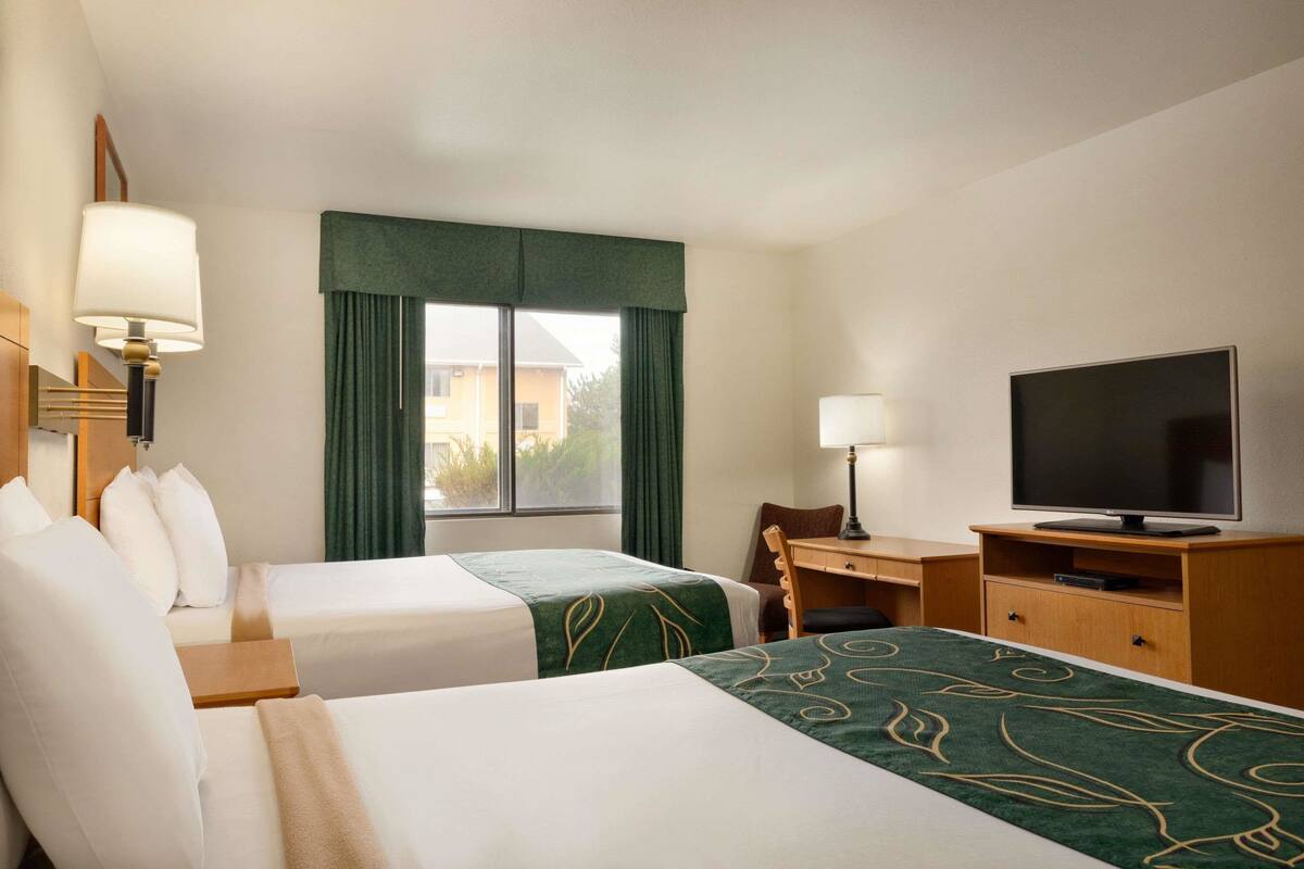 A hotel room with two beds, a desk with a television, and a window with curtains.