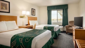 A hotel room with two beds, a desk with a lamp, a chair, a television, and a window with curtains.