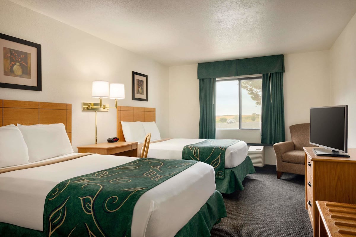 A hotel room with two beds, a desk with a lamp, a chair, a television, and a window with curtains.