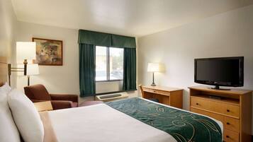 A hotel room with a large bed, a desk with a television, a chair, and a window with curtains.
