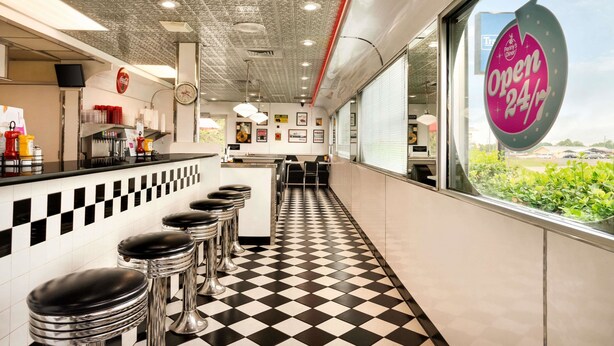 A diner with a checkered floor, bar stools, a Coca-Cola sign, and a window with a view of greenery.