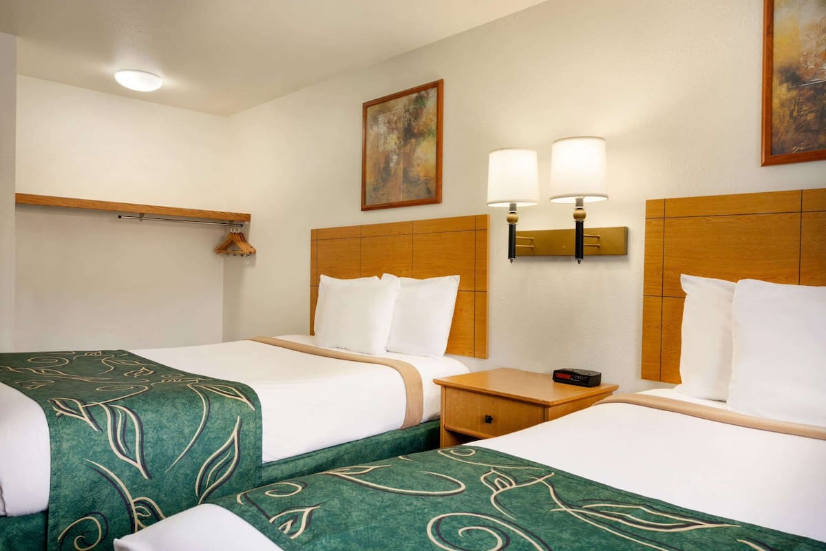 A hotel room with two beds, a wooden headboard, a nightstand, a lamp, and a painting on the wall.