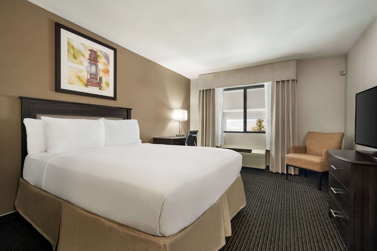 A hotel room with a large bed, a desk, a chair, a television, and a window with curtains.