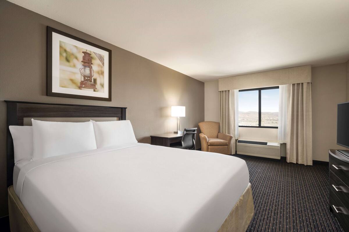 A hotel room with a large bed, a desk, a chair, a television, and a window with curtains.