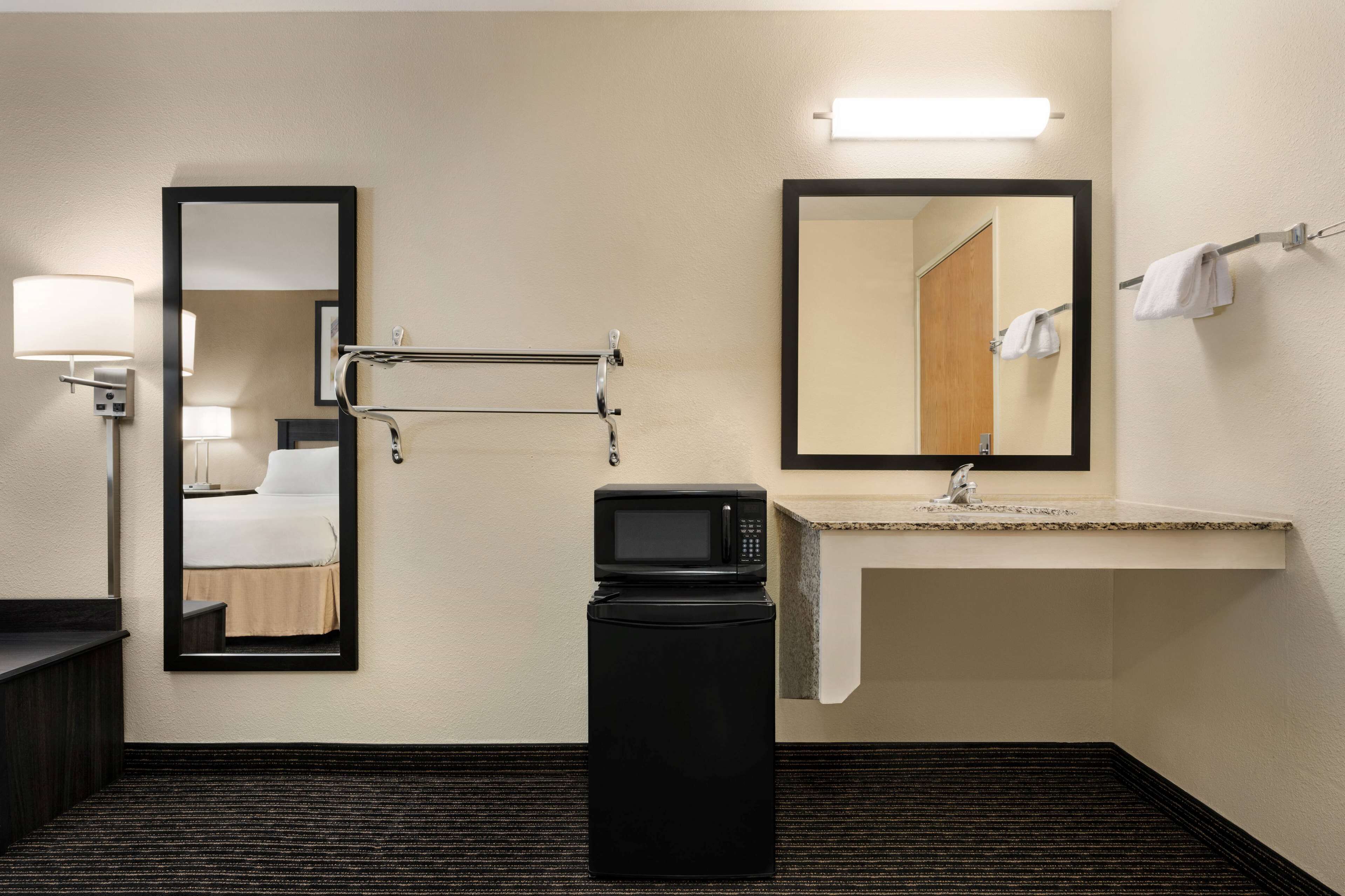 A hotel bathroom with a bed, a sink, a mirror, a microwave, and a trash bin.