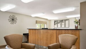 A reception area with a wooden counter, two leather chairs, a decorative wall piece, and framed artwork. - Baymont by Wyndham Elko (Elko)