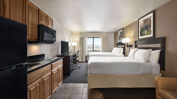A hotel room with a kitchenette, two beds, a TV, and a large window with a view. - Baymont by Wyndham Elko (Elko)