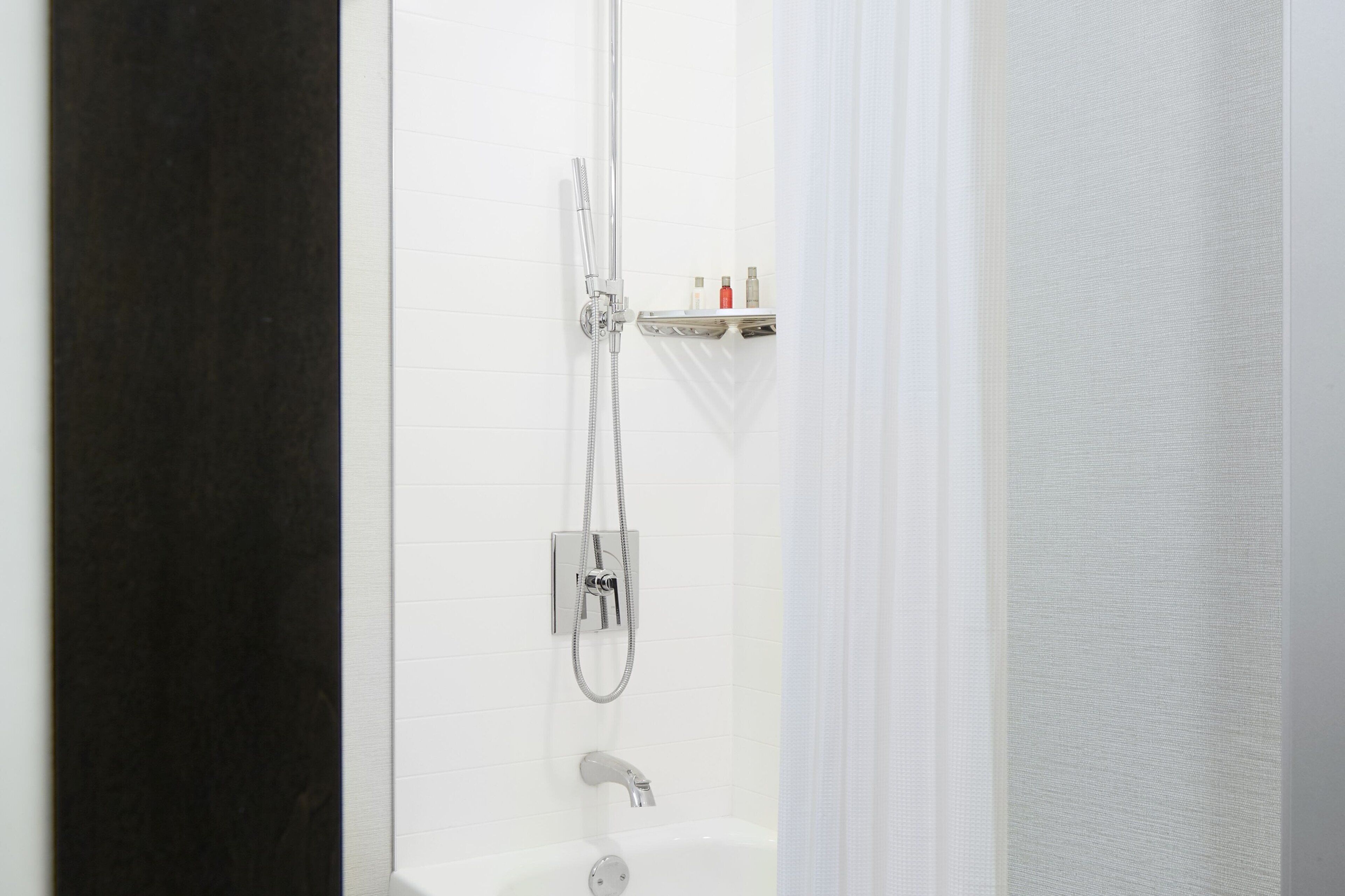 Un baño moderno con ducha, bañera y repisas con artículos de aseo.