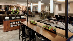 Un moderno vestíbulo de hotel con una zona de bar, áreas de estar y una escalera que sube a un nivel superior.