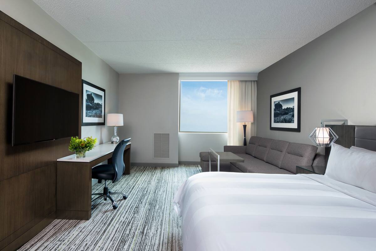 A hotel room with a bed, a desk with a chair, a sofa, a TV, and framed pictures on the walls.