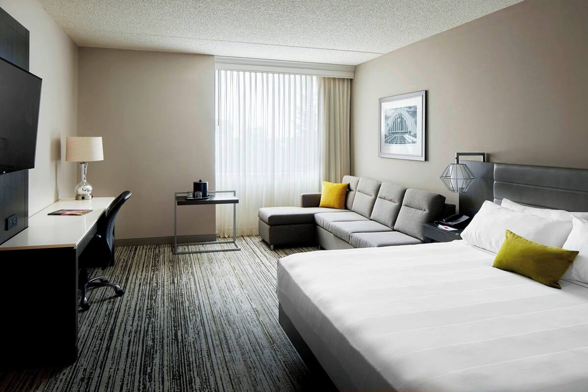A hotel room with a bed, a desk, a chair, a sofa, and a television.