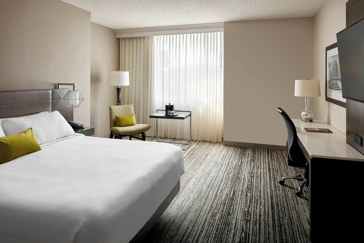 A hotel room with a large bed, a desk, a chair, a TV, and a window with curtains.
