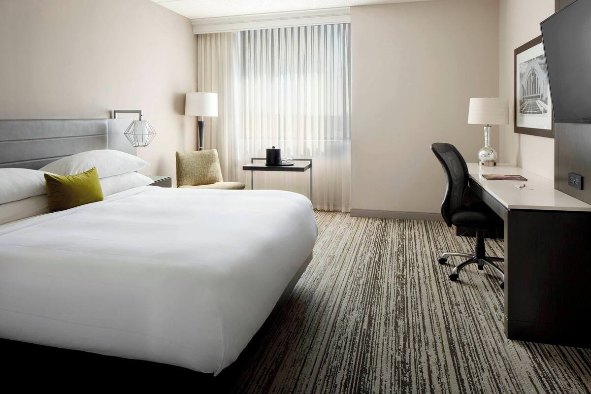 A hotel room with a large bed, a desk, a chair, a small table, and a TV.