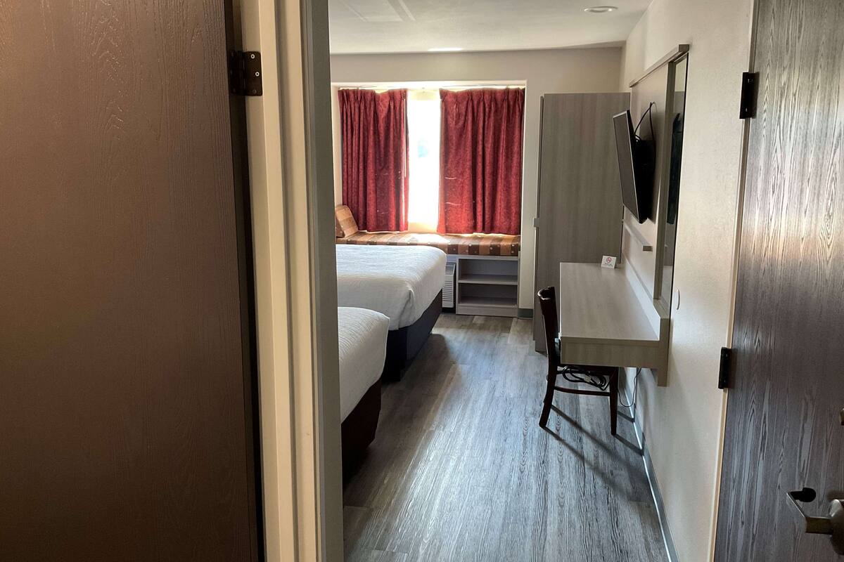Ein Hotelzimmer mit zwei Betten, einem Schreibtisch, einem Stuhl, einem Fernseher und einem Fenster mit Vorhängen.