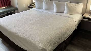 A neatly made bed with white linens and pillows, a bedside table with a phone, and a bench with a patterned cover.