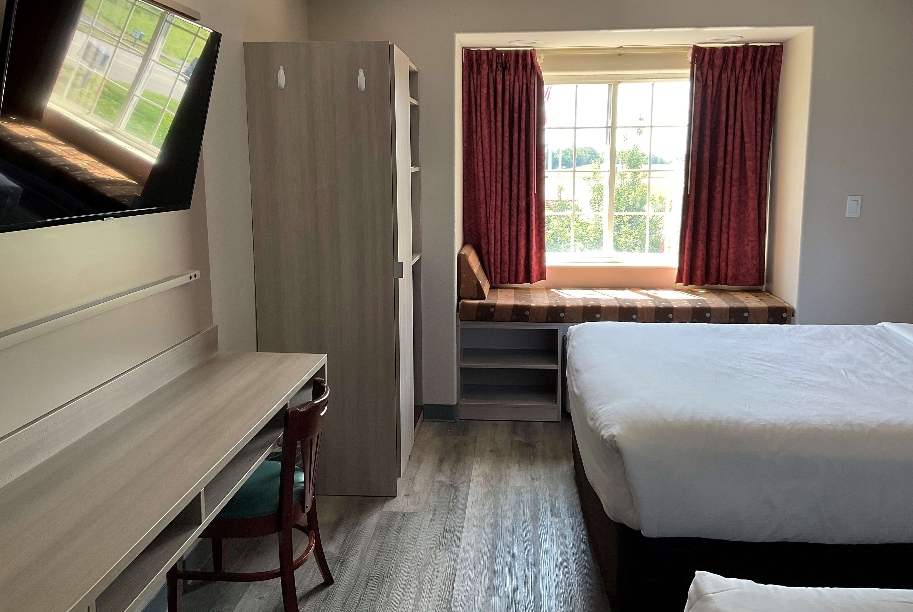 A bedroom with a bed, a desk, a wardrobe, and a window with curtains.