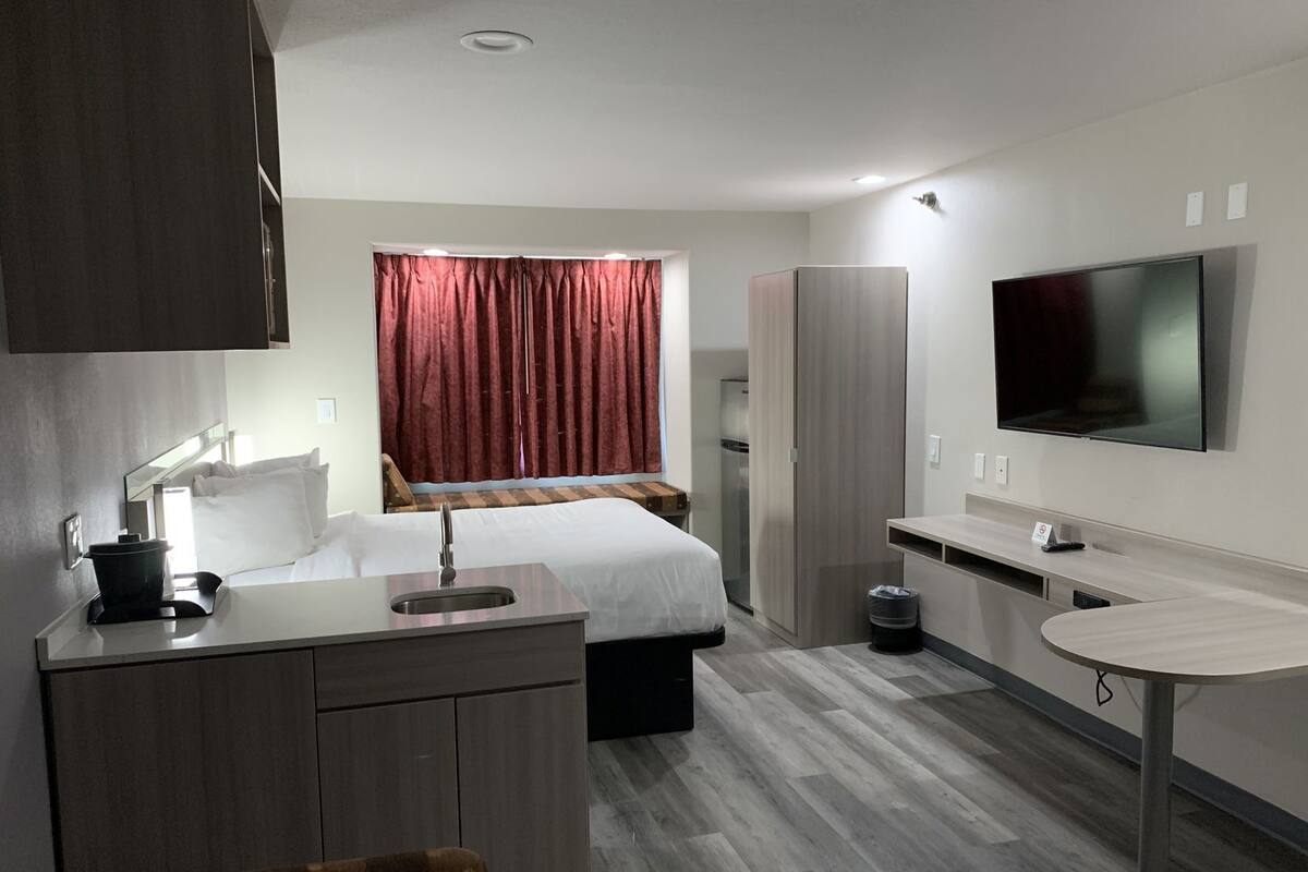 Ein modernes Hotelzimmer mit Bett, Schreibtisch mit Waschbecken, Fernseher und Kleiderschrank.