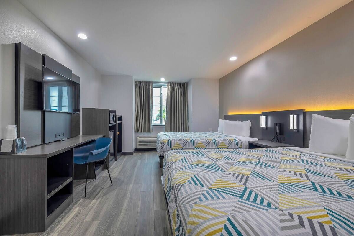 A hotel room with two beds, a desk, a chair, a TV, and a window with curtains.