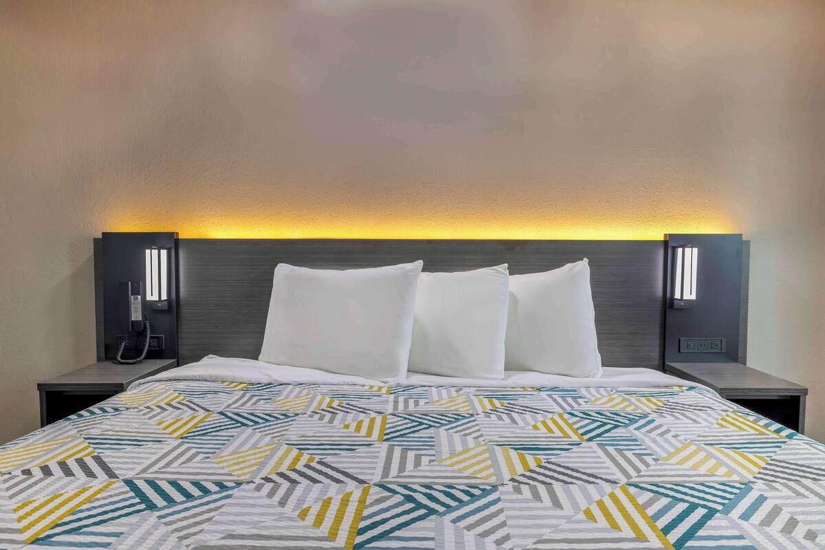 A hotel room with a bed, two bedside tables, and a wall-mounted phone.