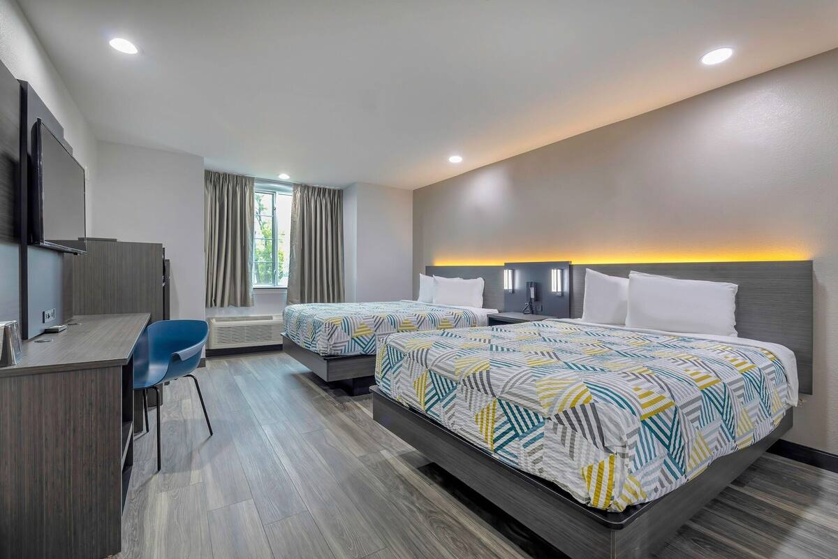 A hotel room with two beds, a desk, a chair, and a window with curtains.