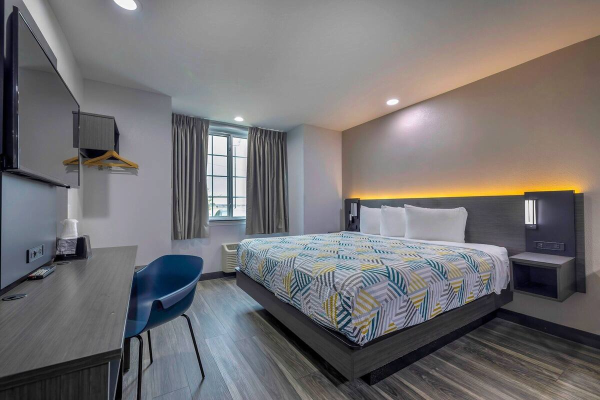 A hotel room with a bed, a desk, a chair, a TV, and a window with curtains.
