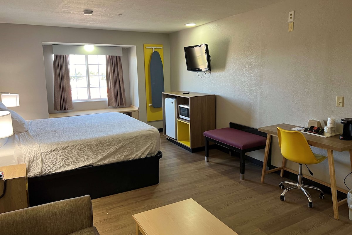 Een hotelkamer met een bed, bureau, stoel, televisie en een kleine kitchenette.