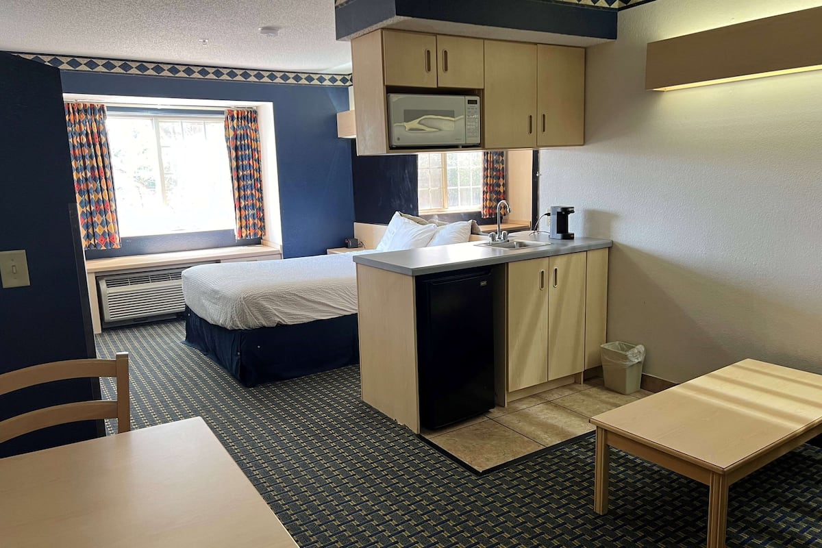 Een compacte hotelkamer met een bed, een kitchenette, een eettafel en een raam met gordijnen.