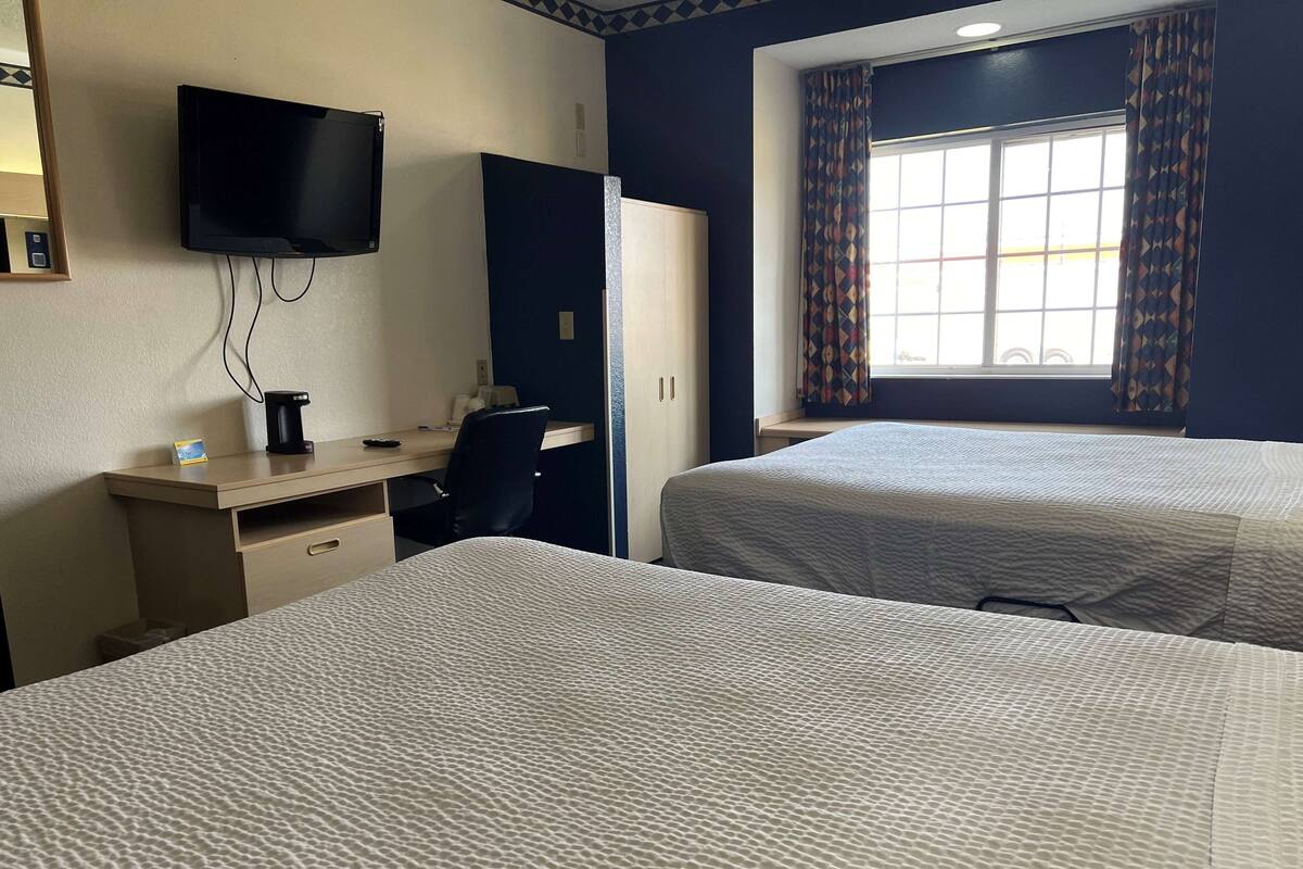 Hotelkamer met twee bedden, een bureau met stoel, een aan de muur bevestigde televisie en een raam met gordijnen met patroon.